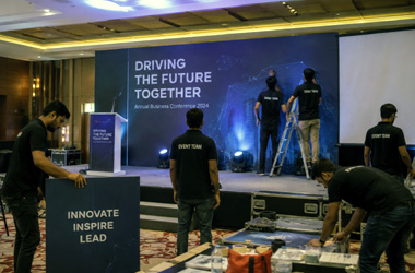 Advertisement Services Professional event branding team setting up exhibition displays, conference stage, promotional branding materials, and event infrastructure at a modern corporate venue.